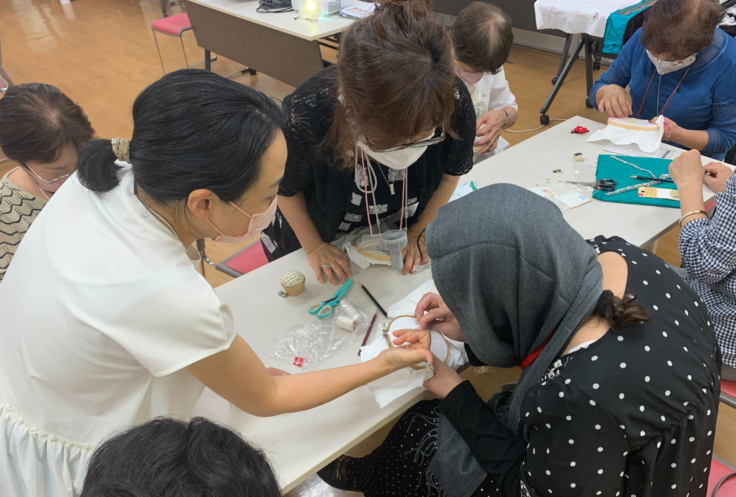 身を乗り出して、講師（手前・右）が刺繍する手元をのぞき込む参加者らの写真