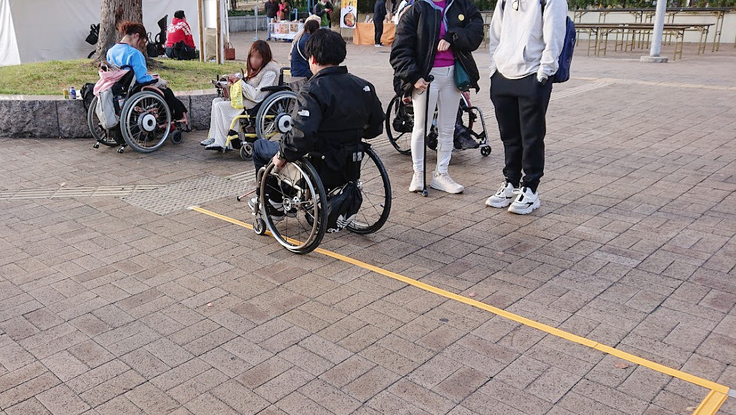 床に貼られたココテープを体験する、車いすユーザーの男性。