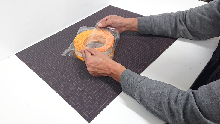 白い作業台の上に黒いカッターマットを置き、３メートル巻きのココテープを透明な袋に梱包している写真