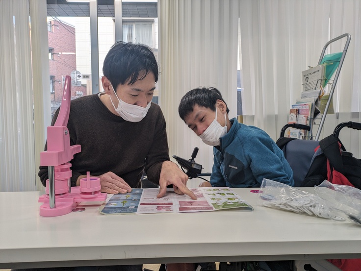 岩切と介助者がバッヂマシンの取扱説明書と睨めっこ。