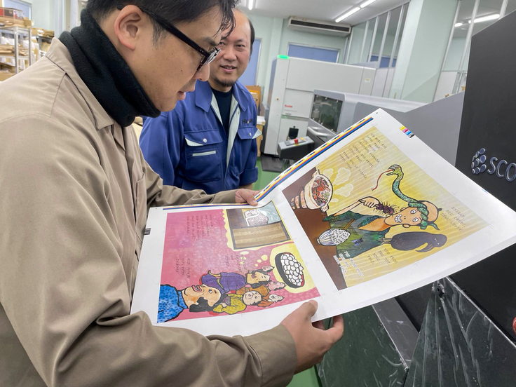 印刷したての誌面を触る昇吉代表理事