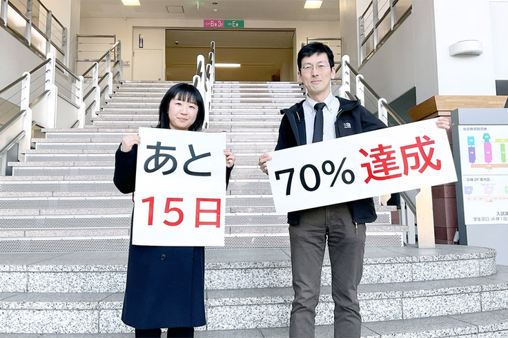 「あと15日」「70%達成」という紙を見せているところ
