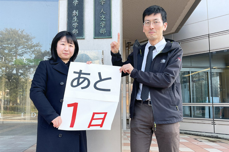 「人文学部」の看板の前で、「あと1日」と書かれた紙を持っているところの写真