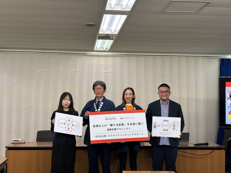 厚生労働省の記者会見室の机の前に4人の登壇者が並び、クラファンを紹介するパネルを手に持ちながらフォトセッションを行なっています。