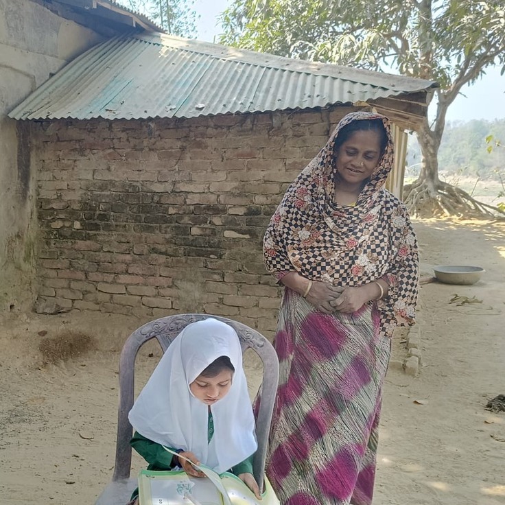 教科書を開くヌール・ハリマさんを見守る母親