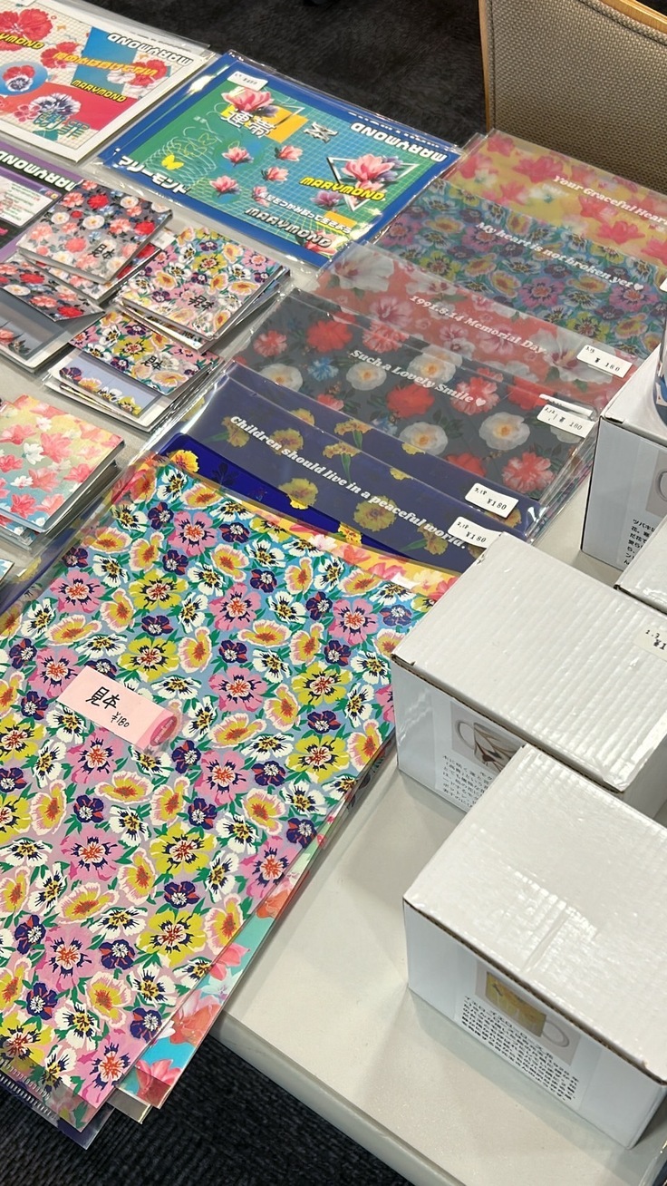 マリ―モンドの物販の様子。机にクリアファイルやカップの入った箱が並べられている。